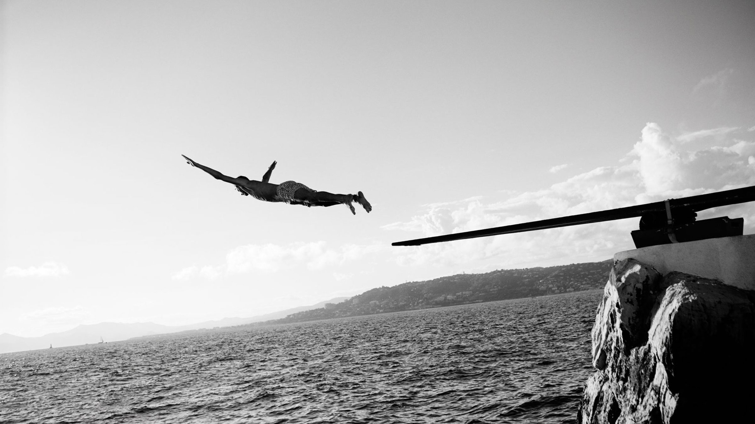 Black and white photo of a diver leaping from the rocks at Eden-Roc